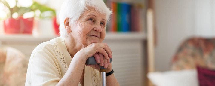 Eine ältere Frau mit Stock sieht fröhlich in die Ferne