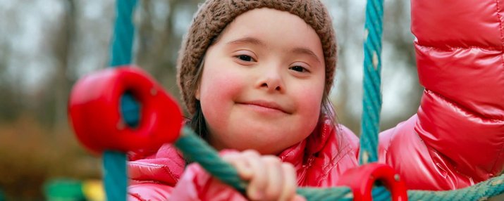 Ein Mädchen mit Down-Syndrom spielt auf einem Klettergerüst.