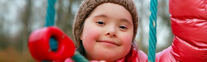 Ein Mädchen mit Down-Syndrom spielt auf einem Klettergerüst.